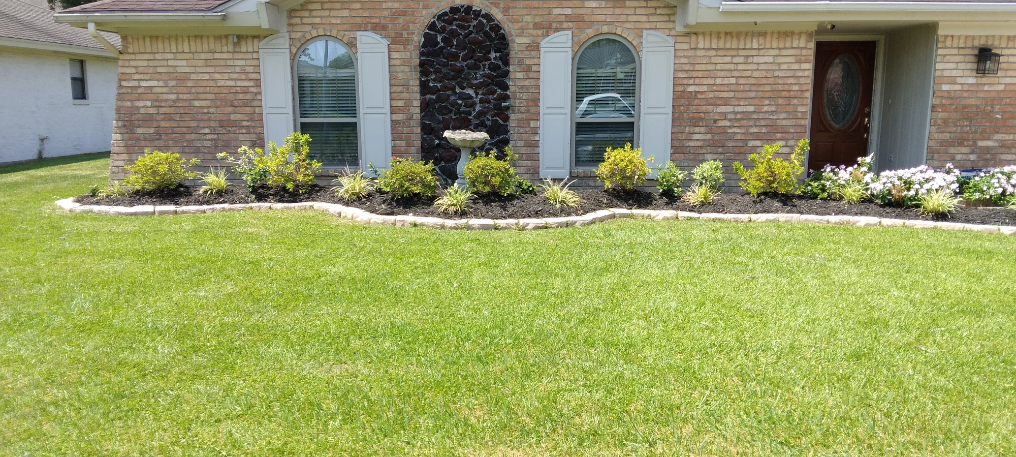 Freshly landscaped garden beds and lawn in front of a brick home